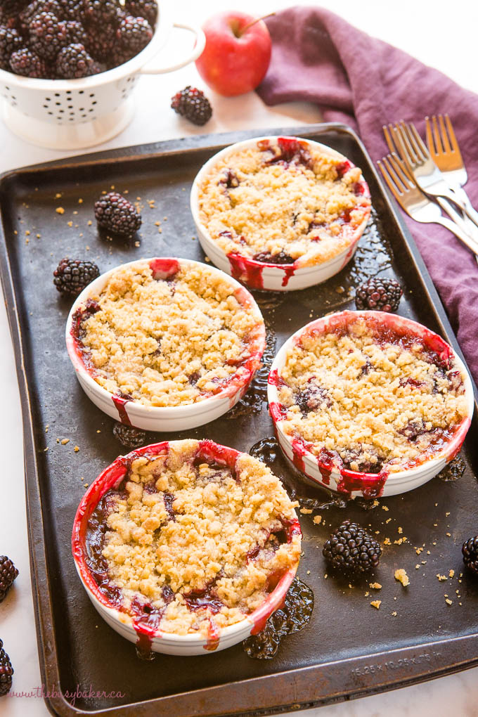 apple blackberry crumble in white ramekins on a dark baking sheet