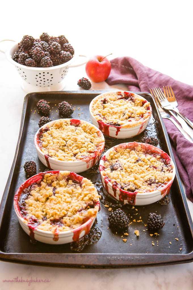 single serving apple blackberry crumble on a dark baking sheet with fresh blackberries