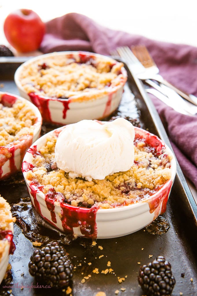 single serving of apple blackberry crumble in a white ramekin with a scoop of vanilla ice cream