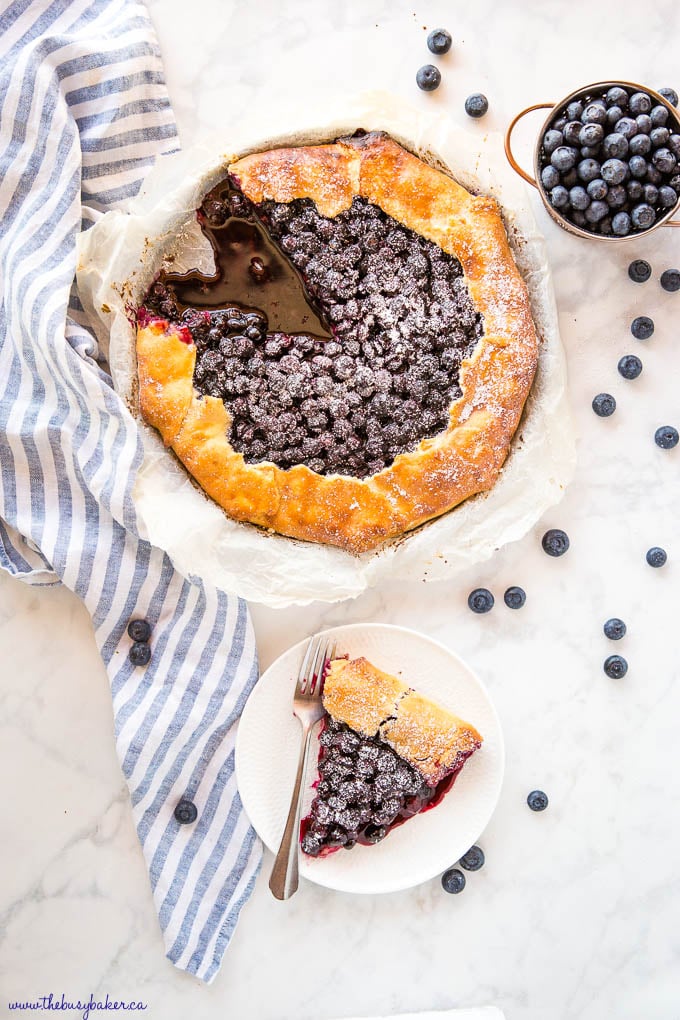 overhead image: blueberry galette with a slice missing, slice of blueberry galette on white plate with a fork