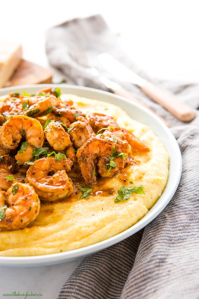 creamy polenta in blue bowl with saucy cajun shrimp and fresh herbs