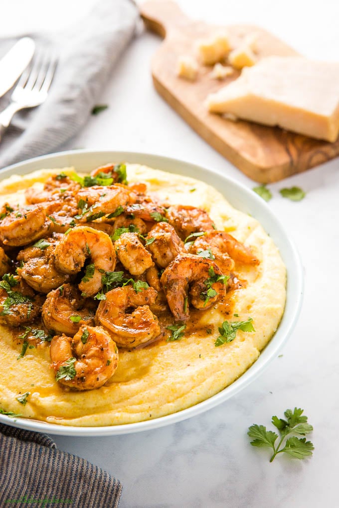 cajun shrimp over creamy cheesy polenta with fresh herbs in blue bowl