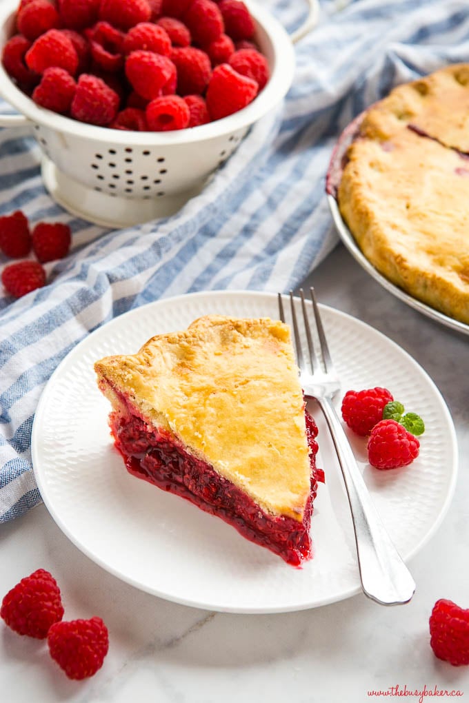 slice of raspberry pie on white plate with fork and fresh raspberries