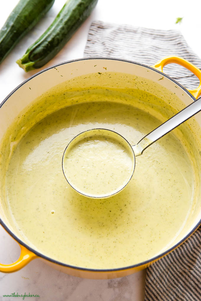 ladle of creamy zucchini soup in yellow pot