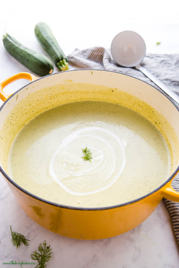 creamy zucchini soup in yellow pot with cream and fresh dill