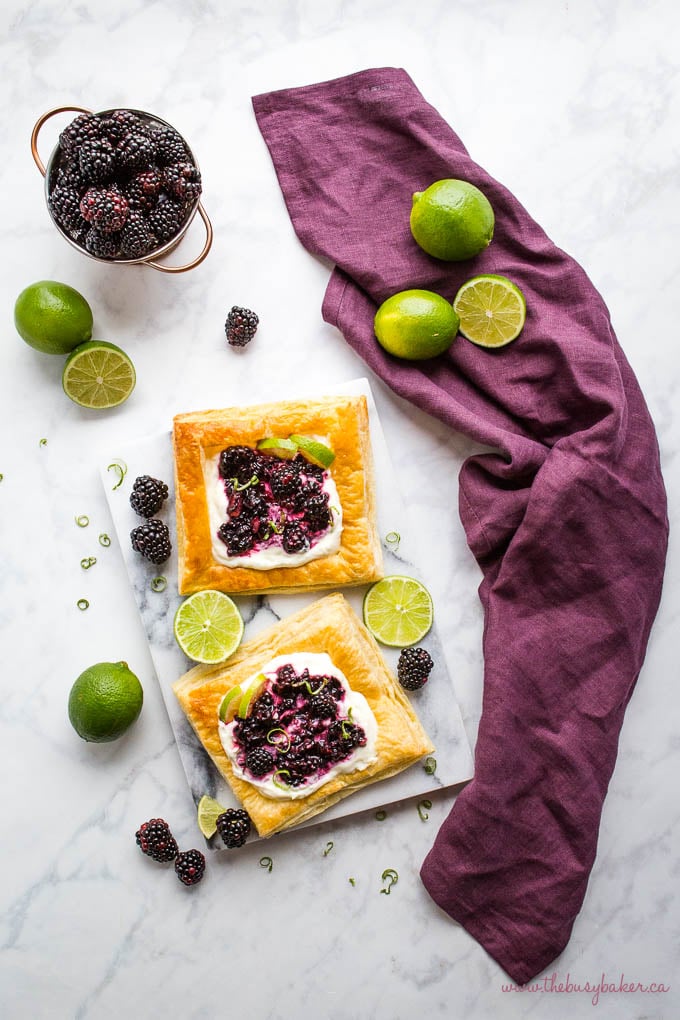 overhead image: puff pastry danishes with creamy filling, lime, and fresh blackberries on a marble background with a purple kitchen towel