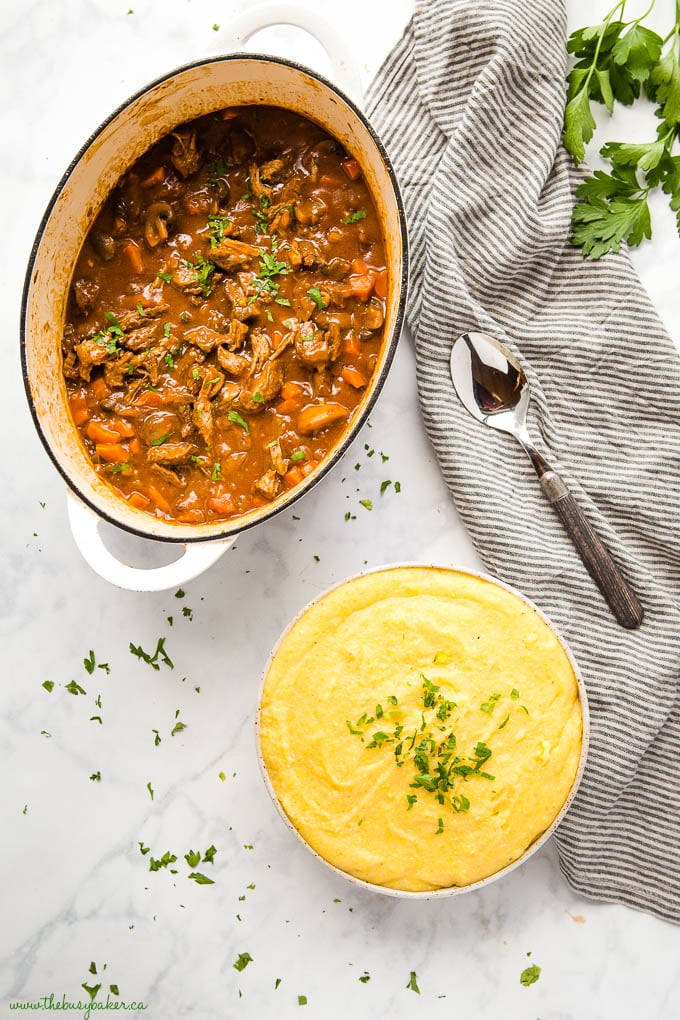 overhead image: white pot with braised beef stew with carrots and mushrooms and a bowl of polenta with fresh herbs