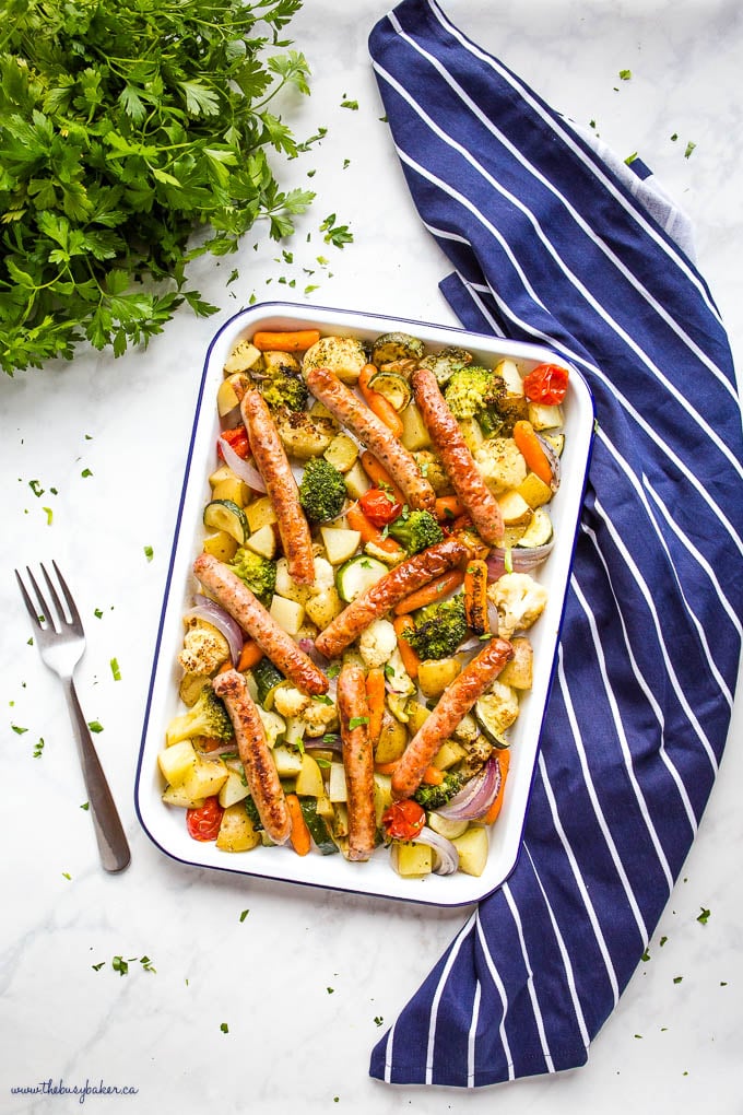 overhead image:: white enamel baking sheet with blue rim, with chicken sausages, potatoes, broccoli, cauliflower, zucchini, carrots, and tomatoes