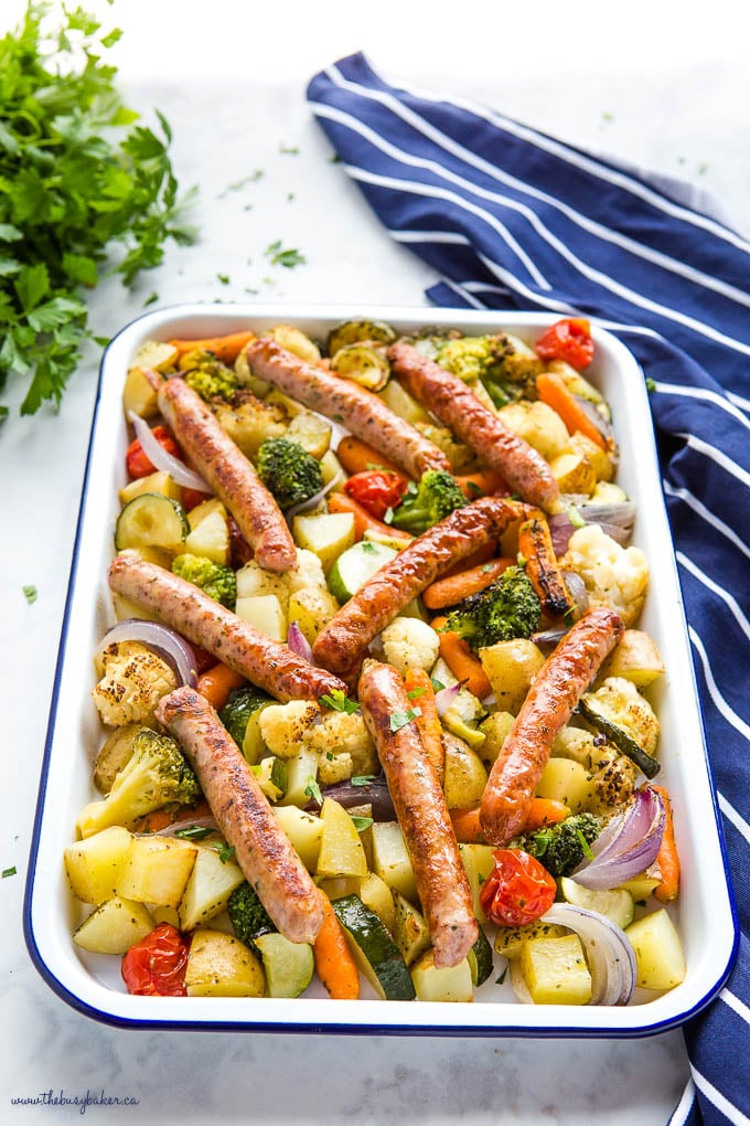 sheet pan dinner with chicken sausages, potatoes, and veggies on white enamel baking sheet with blue rim