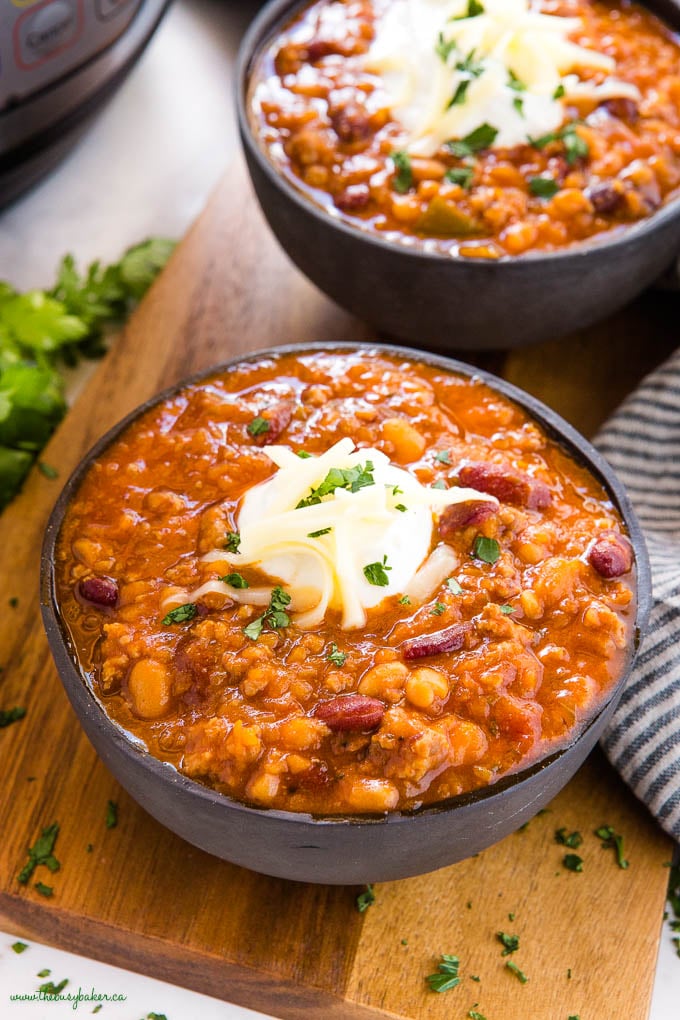 black bowl with instant pot beef and bean chili, with sour cream, cheese and herbs