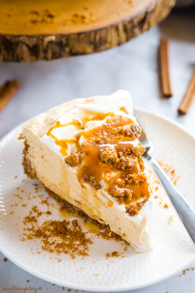slice of no bake pumpkin cheesecake on white plate with cookie crumbs and caramel sauce