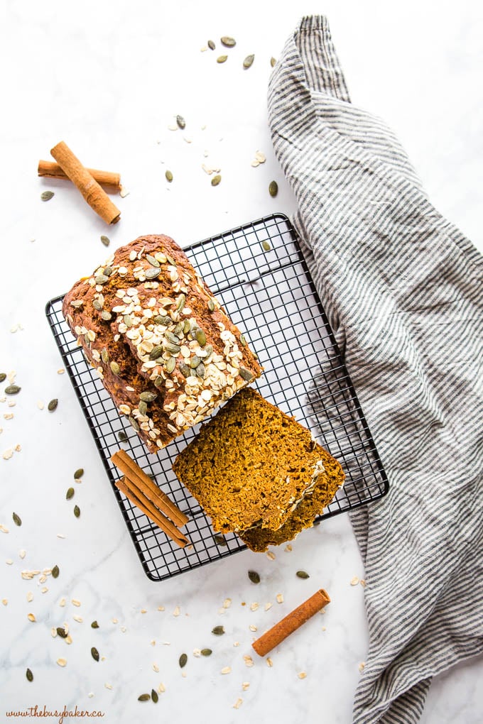 overhead image: pumpkin oat bread on black wire rack with cinnamon sticks and pumpkin seeds