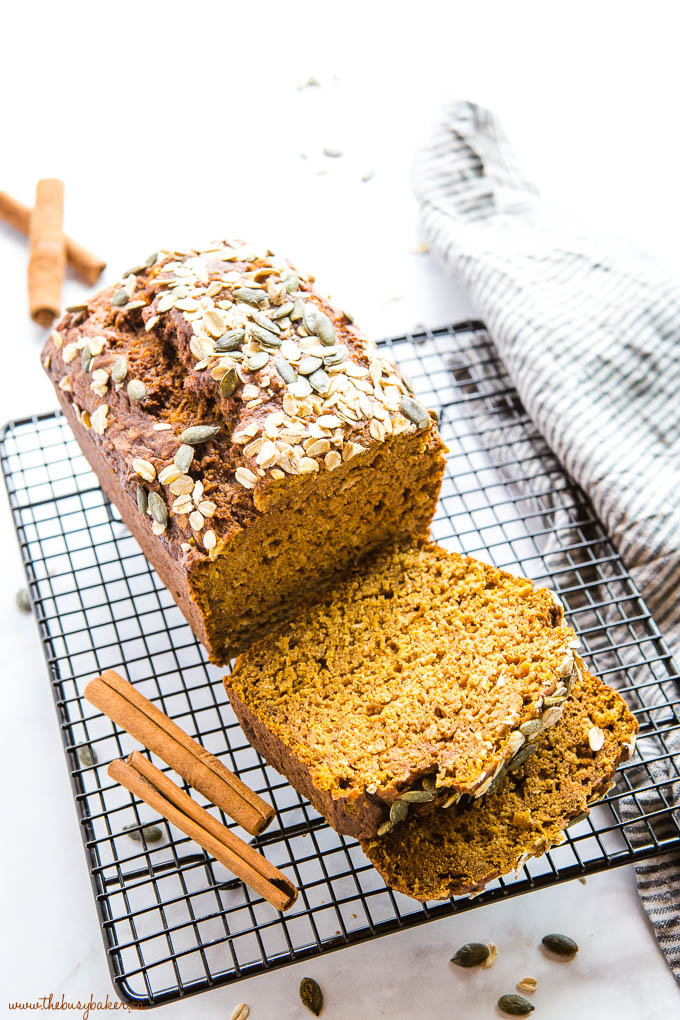 loaf of pumpkin bread cut into slices, with oats, pumpkin seeds, applesauce and cinnamon sticks