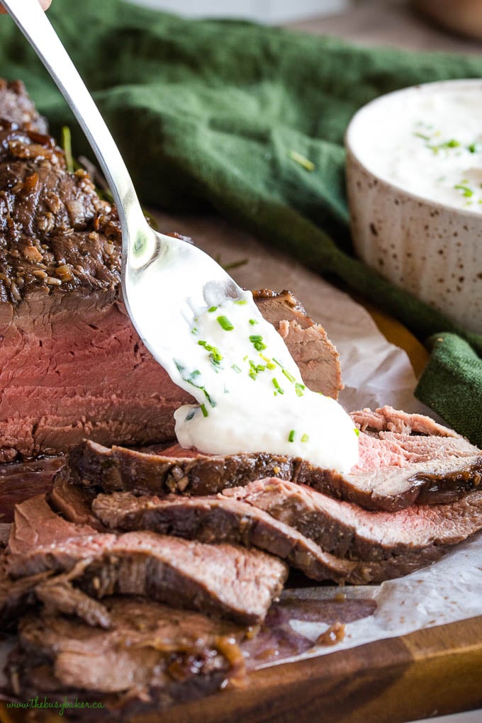 This Best Ever Marinated Beef Tenderloin is perfectly tender & juicy and packed with flavour - Easy to make with a simple marinade and great for the holidays served with horseradish sauce! Recipe from thebusybaker.ca! #holidays #beef #tenderloin #steak #horseradish #sauce #marinade #marinated #meat #roasted #christmas #holidays #newyears #celebration tenderloin slices with a spoonful of horseradish sauce