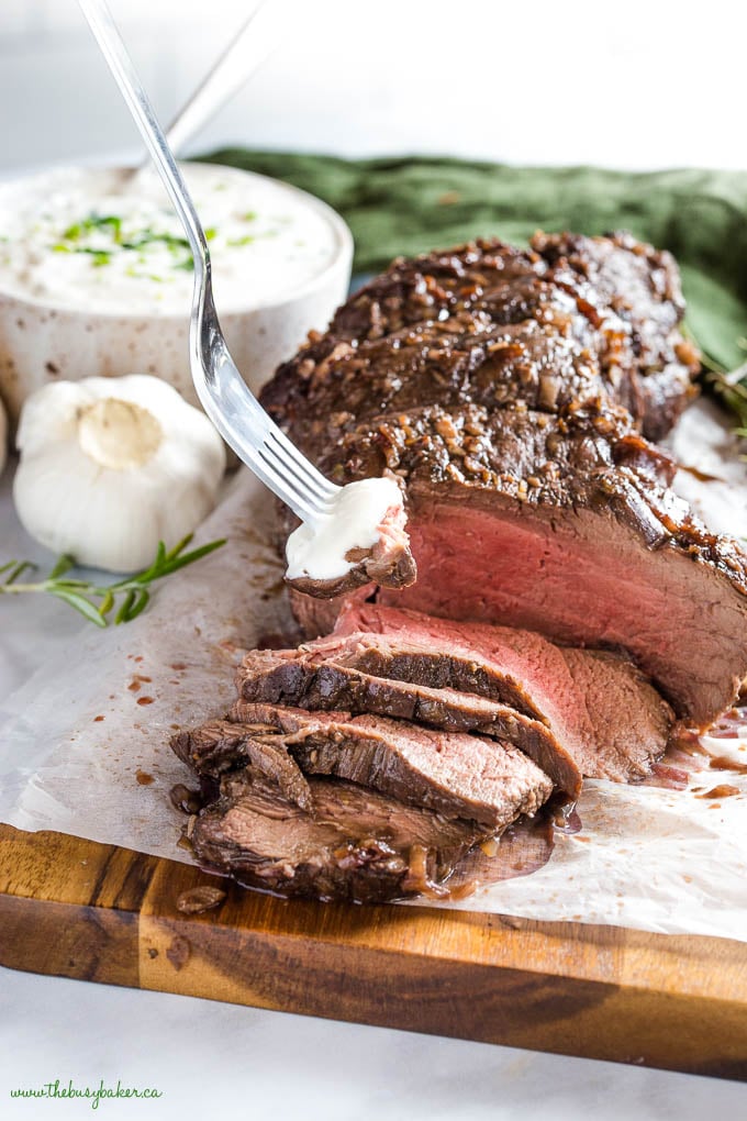 fork lifting a piece roasted tenderloin, medium rare, with horseradish sauce