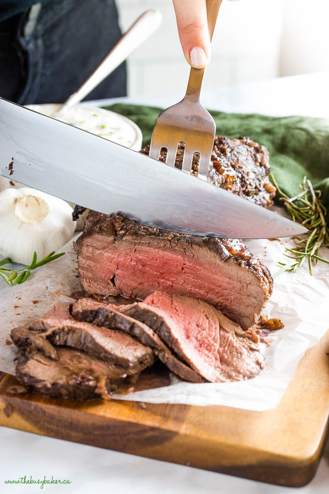 knife and fork slicing roasted medium rare beef tenderloin