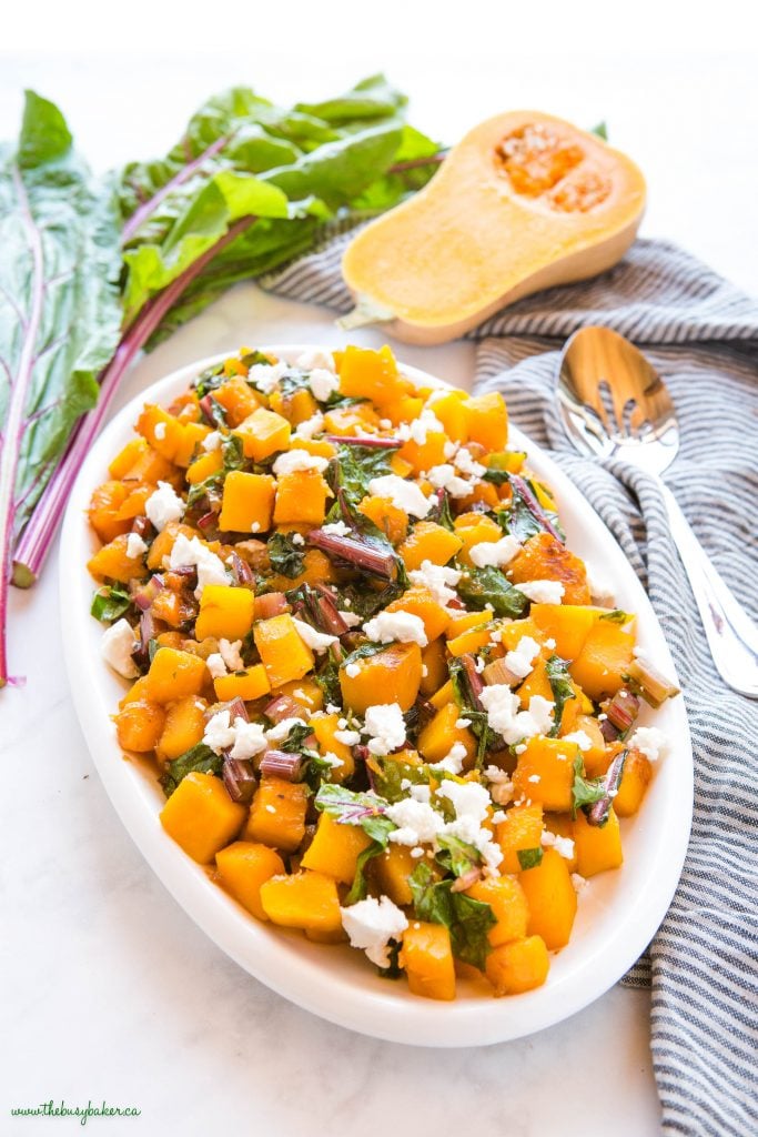 white platter with caramelized butternut squash, greens, and goat cheese