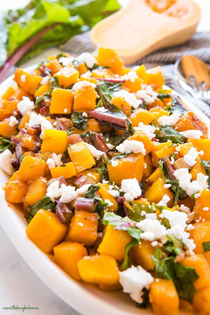 close-up image: caramelized butternut squash with greens and goat cheese on a white platter