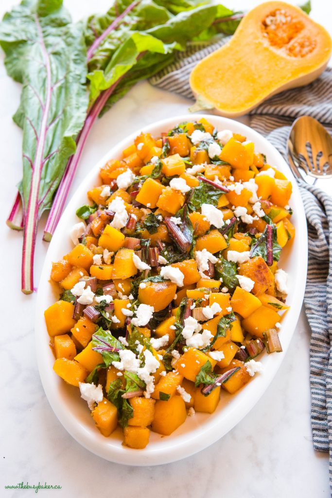 butternut squashed with greens on white platter with goat cheese