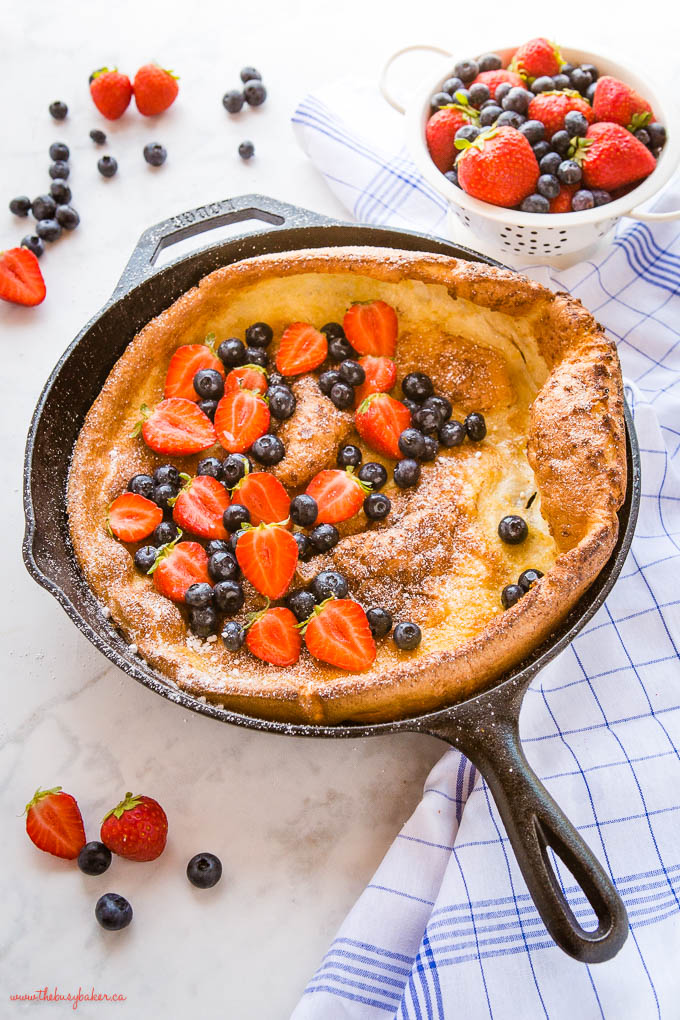 dutch baby pancake in cast iron skillet with fresh berries and powdered sugar