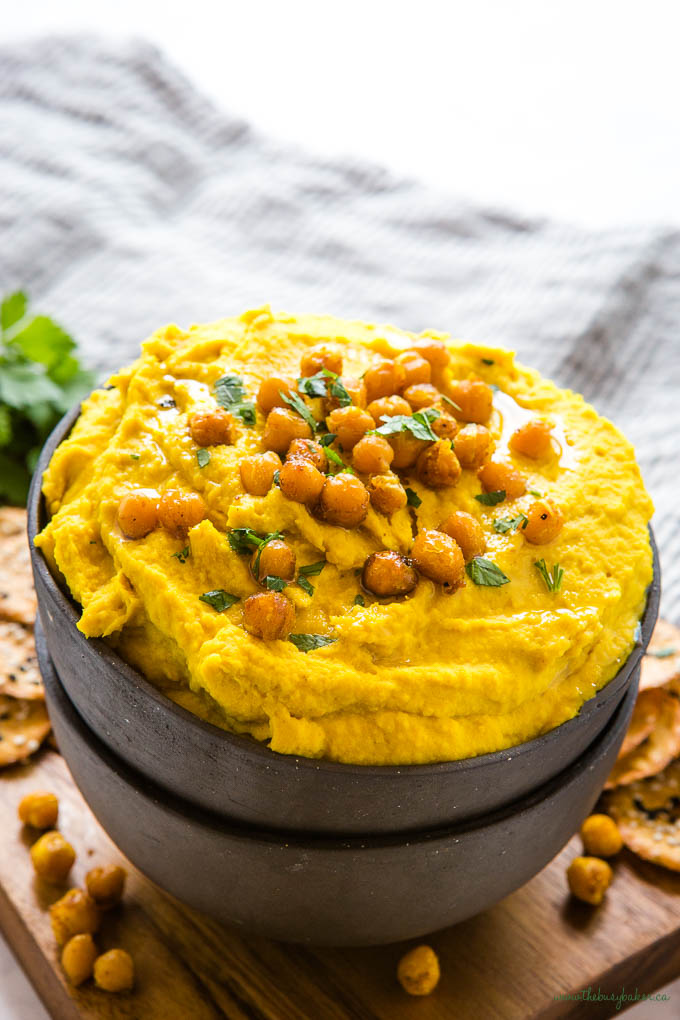 golden turmeric hummus in black pottery bowl with roasted chickpeas and fresh herbs