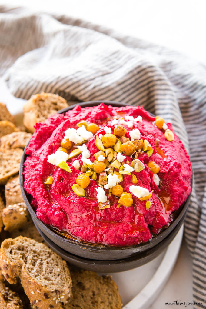pink roasted beet hummus in black bowl with feta and chopped pistachos