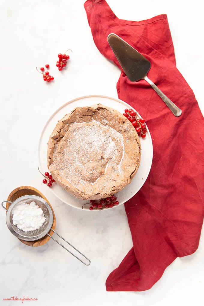 overhead image: flourless chocolate cake with a dusting of powdered sugar and red kitchen towel and berries