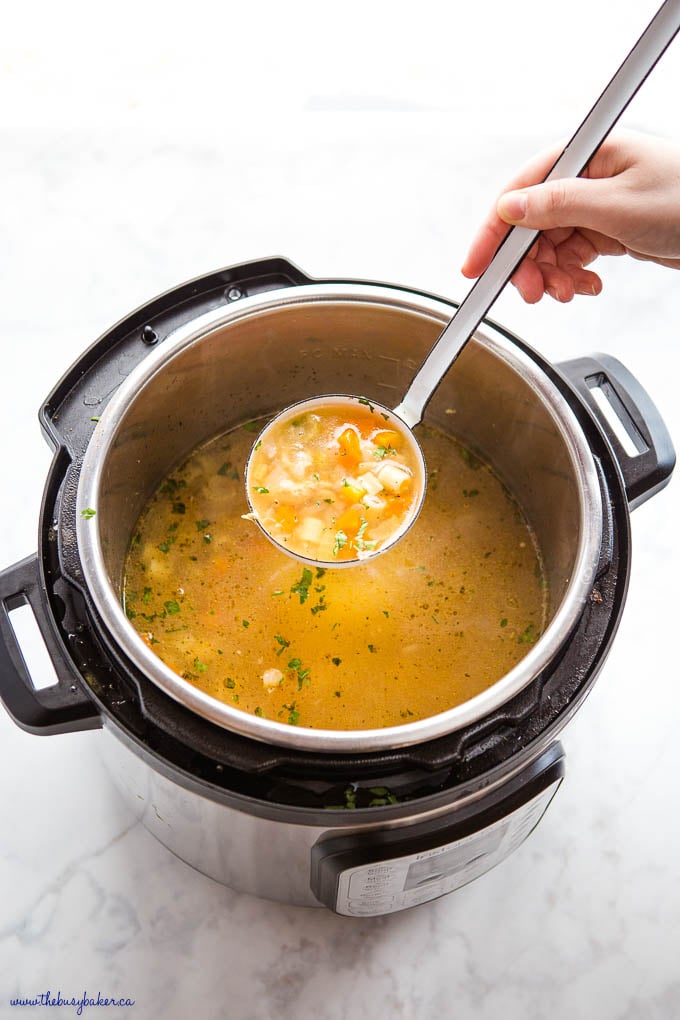 hand holding ladle of chicken noodle soup over the instant pot