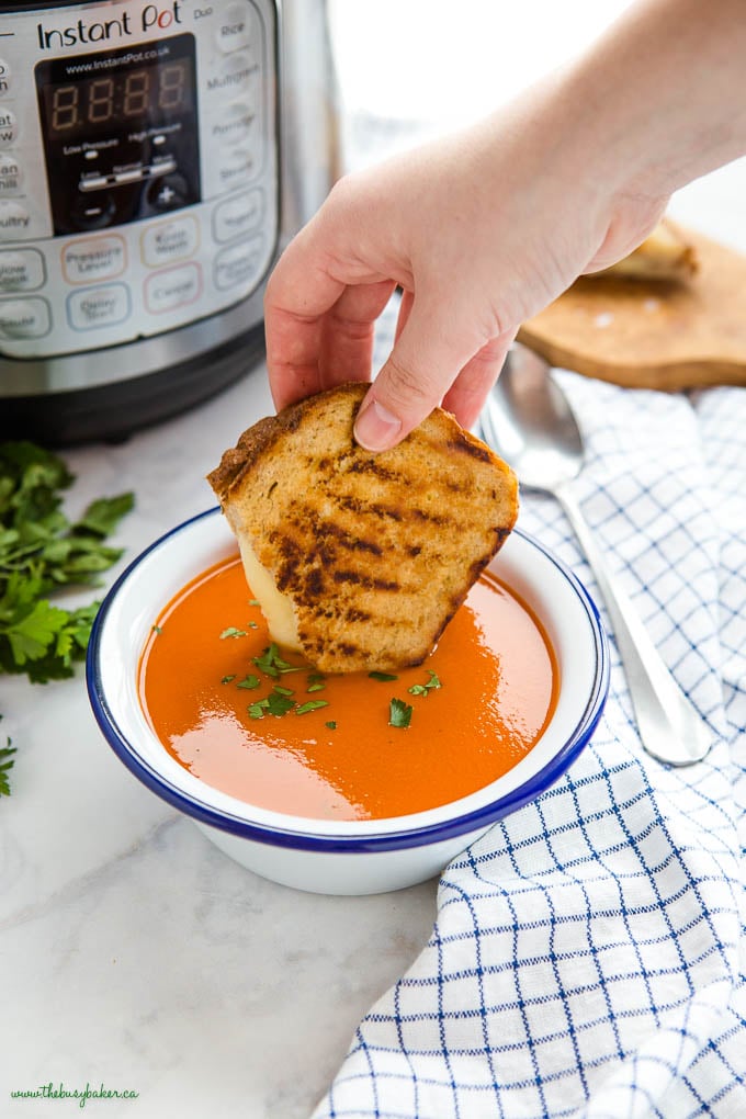 hand dipping a grilled cheese sandwich into tomato soup