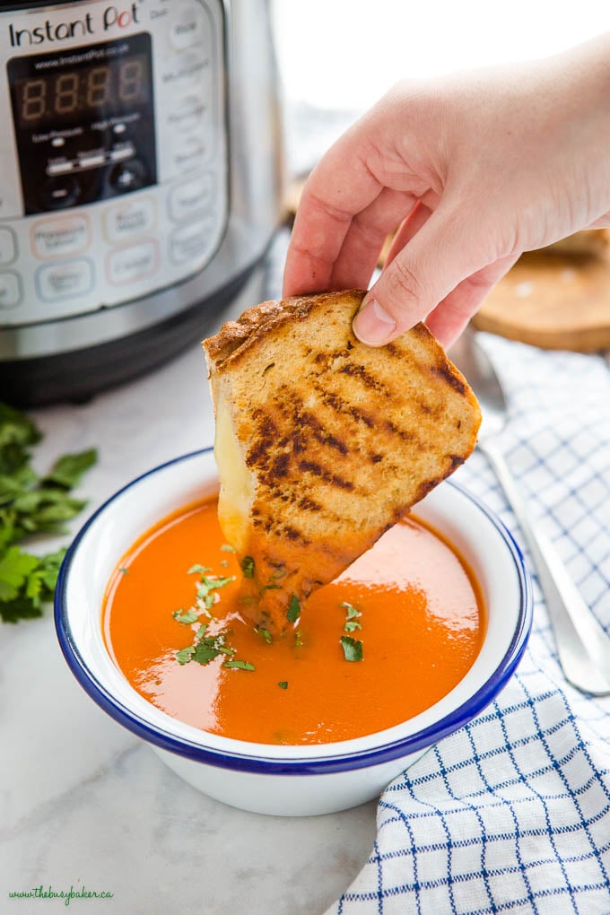 hand dipping grilled cheese sandwich into bowl of tomato soup