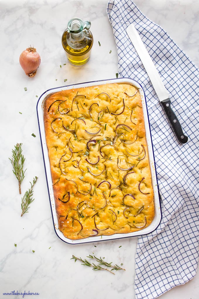 overhead image: pan of rosemary onion focaccia bread with fresh rosemary and olive oil 