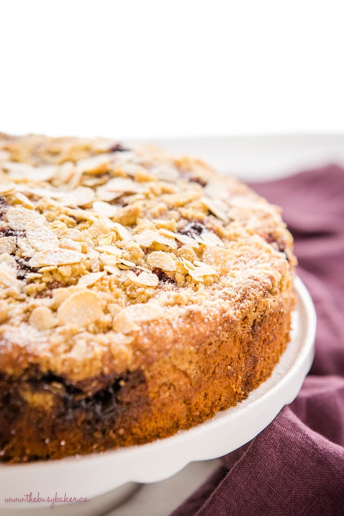 cherry almond coffee cake on white cake stand with slivered almonds and powdered sugar