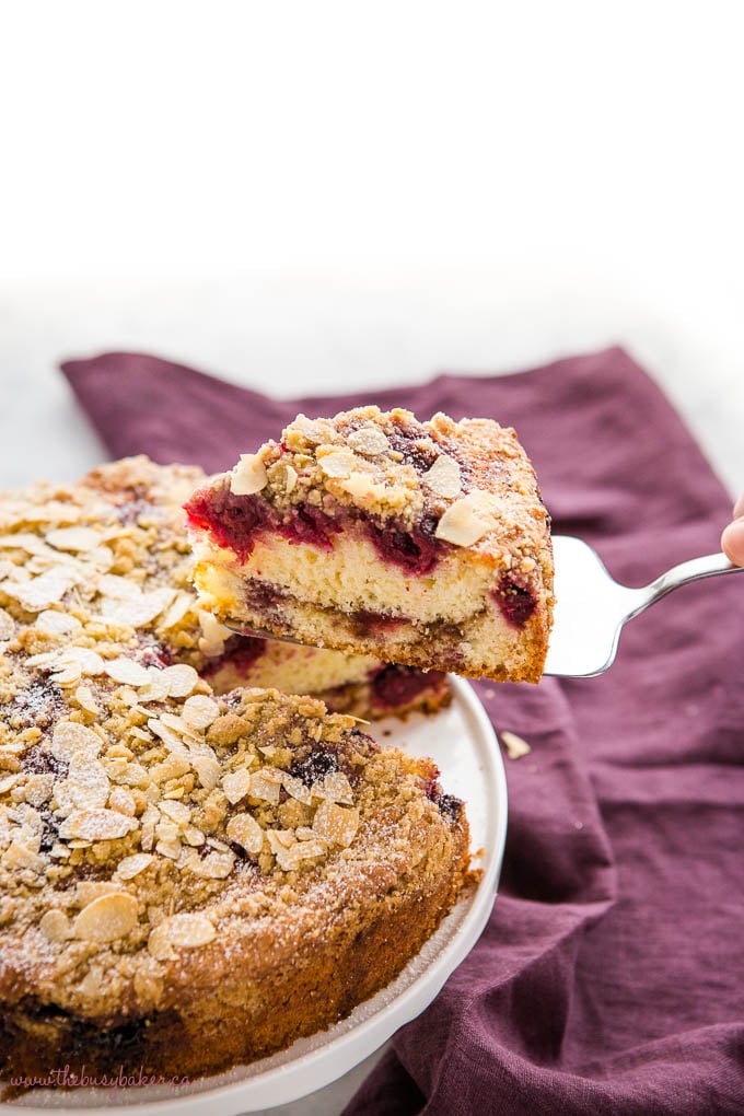 hand lifting slice of cherry almond coffee cake with slivered almonds and powdered sugar