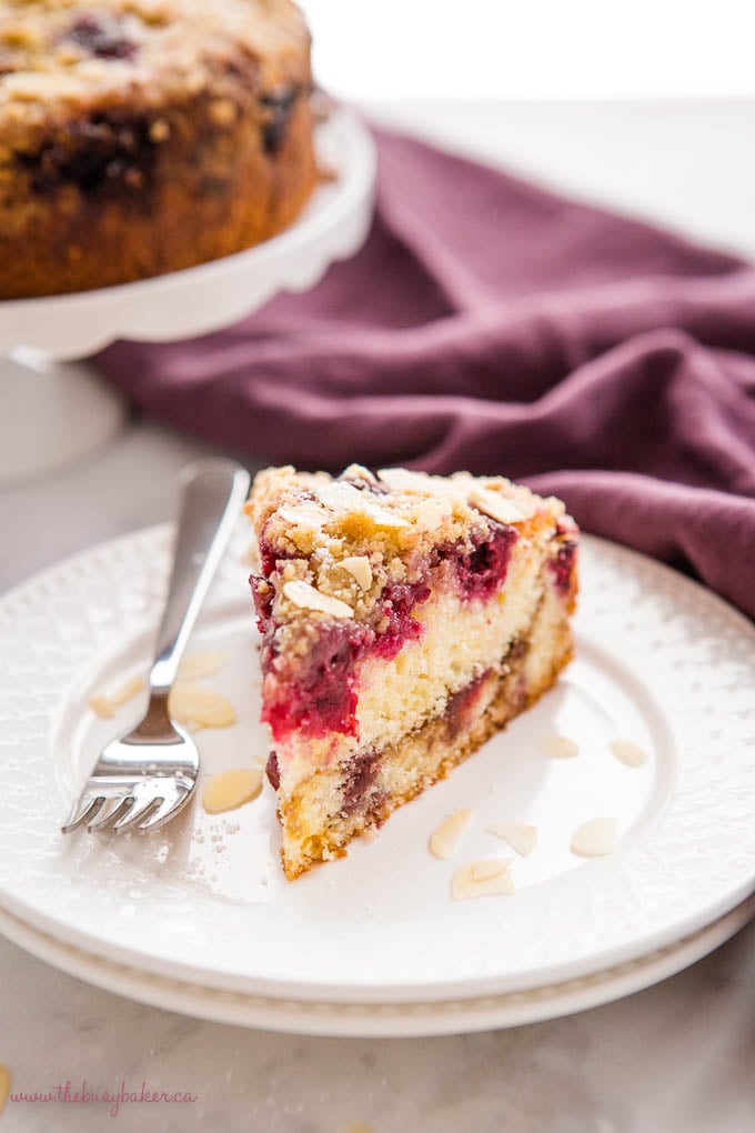 slice of cherry almond coffee cake on white plate with powdered sugar and slivered almonds