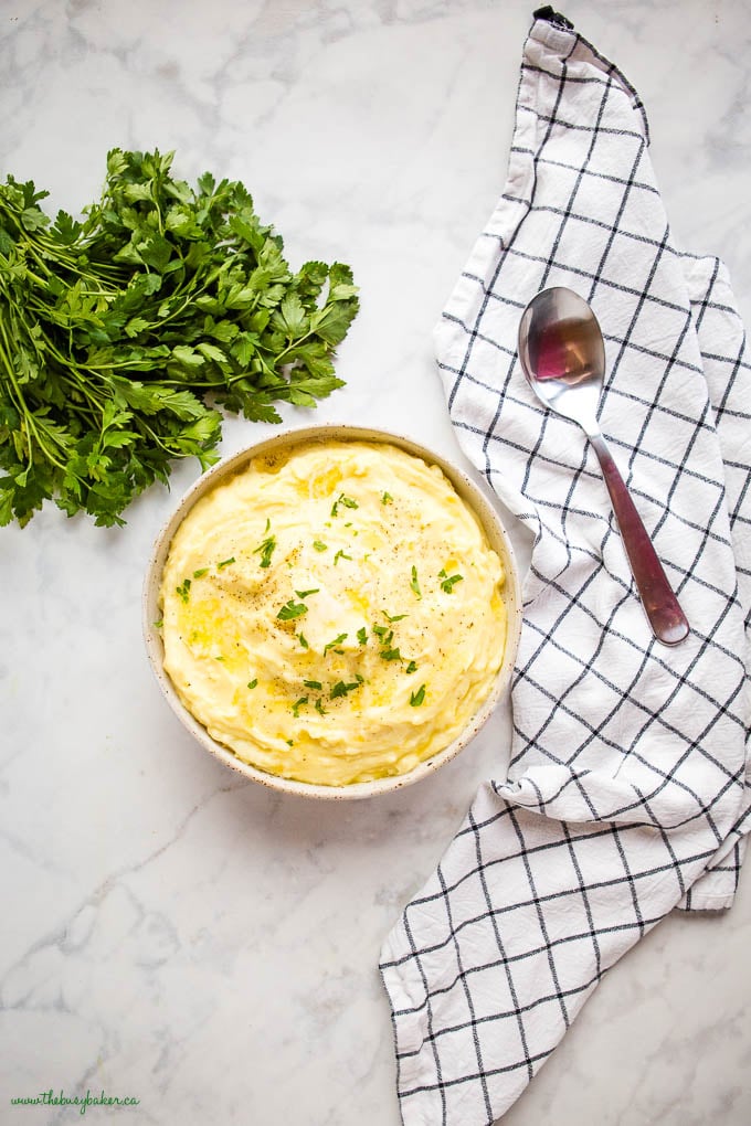 overhead image: mashed potatoes in a bowl with butter and fresh herbs