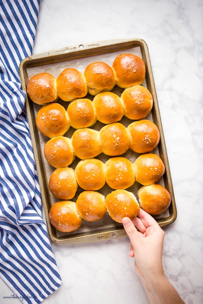 overhead image: hand reaching for a dinner roll, a pan of golden brown dinner rolls