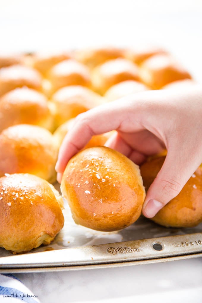 hand reaching for golden brown dinner roll with flaky sea salt on top