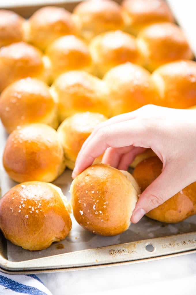 hand reaching for golden brown dinner roll on baking pan