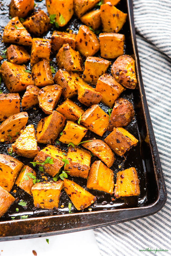 roasted sweet potatoes with chili flakes and honey on a black sheet pan