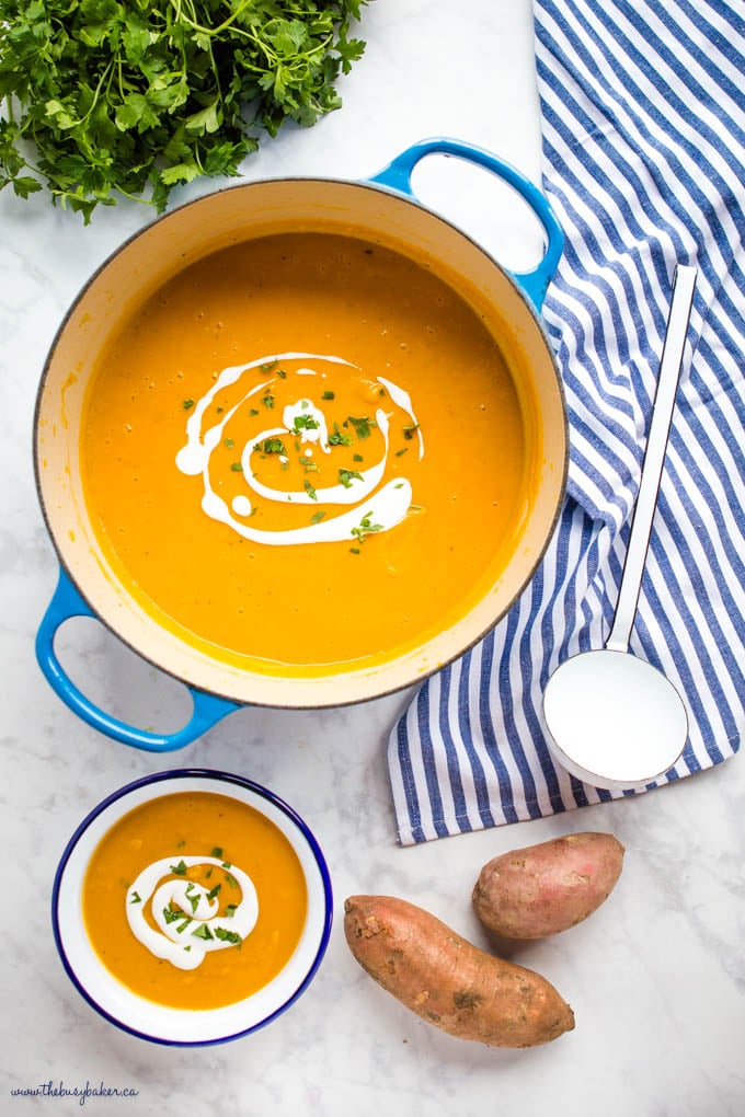 overhead image: sweet potato soup in blue cast iron pot with white ladle and herbs