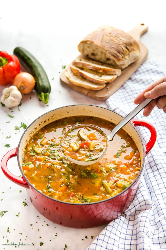 ladle of vegetable soup in red cast iron pot