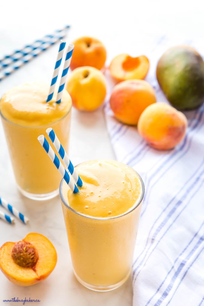 peach mango smoothie in glass with blue striped paper straws