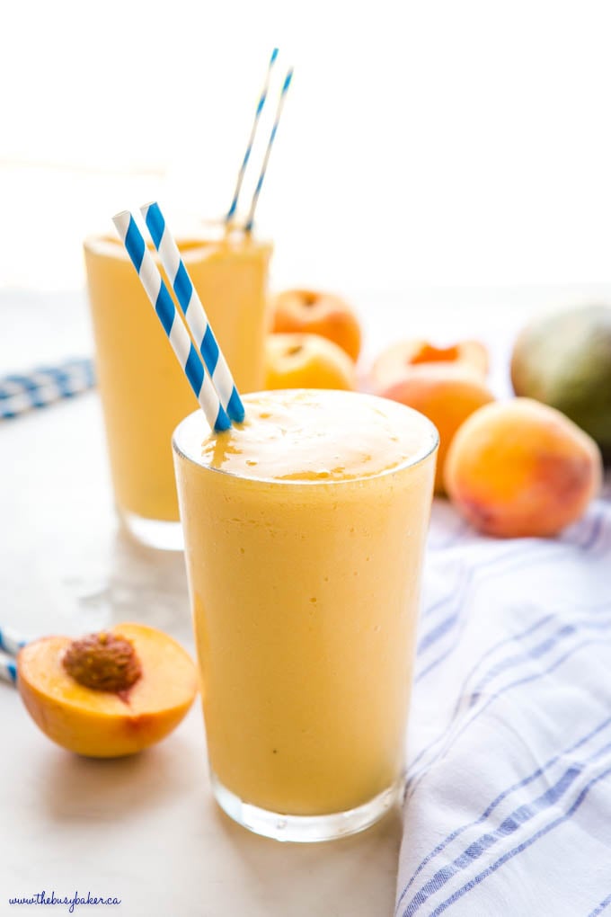 peach mango smoothie in tall glass with blue striped paper straws