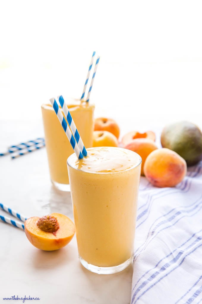 yellow peach mango smoothie in a large glass with blue straws