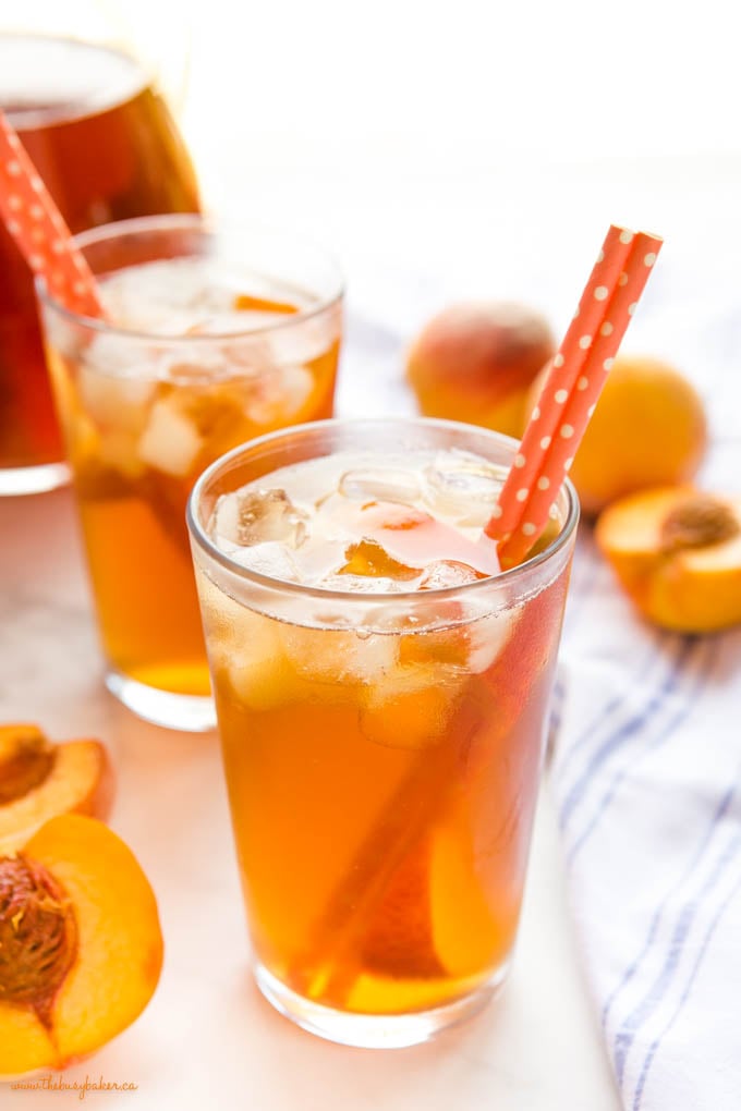 glass of fresh peach iced tea with ice and paper straws