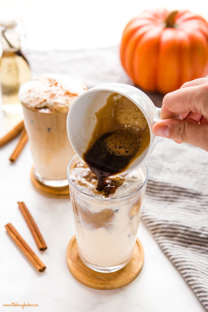 hand pouring espresso over pumpkin spice milk in tall glass