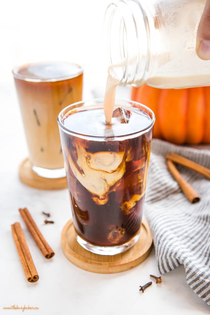 This Starbucks Pumpkin Cream Cold Brew is the perfect pumpkin spice iced coffee drink - easy-to-make cold brew coffee sweetened with a simple pumpkin cream made in a mason jar! Skip the coffee shop and make your favourite Pumpkin Cream Cold Brew at home! Recipe from thebusybaker.ca! #pumpkincreamcoldbrew #pumpkinspicelatte #pumpkinspice #pumpkin #fall #easytomake #coffee #homemade #starbucks #copycat pouring pumpkin sweet cream over cold brew coffee in tall glass with ice