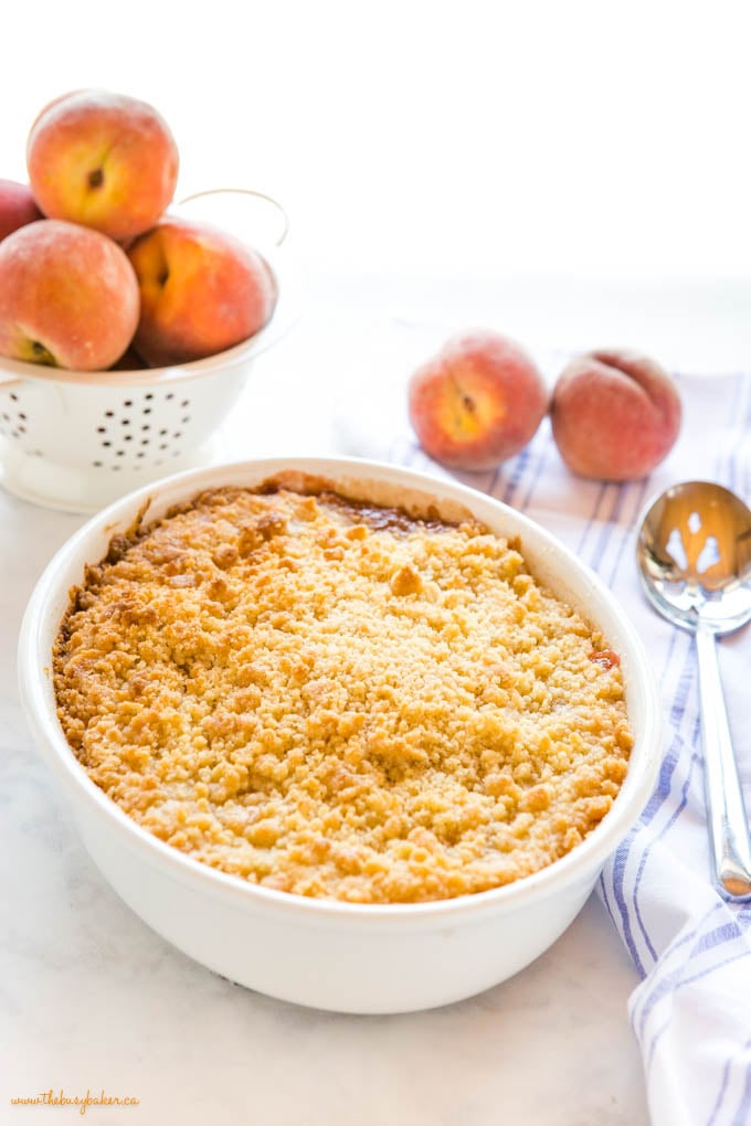 fresh peach crumble in white oval baking dish with serving spoon
