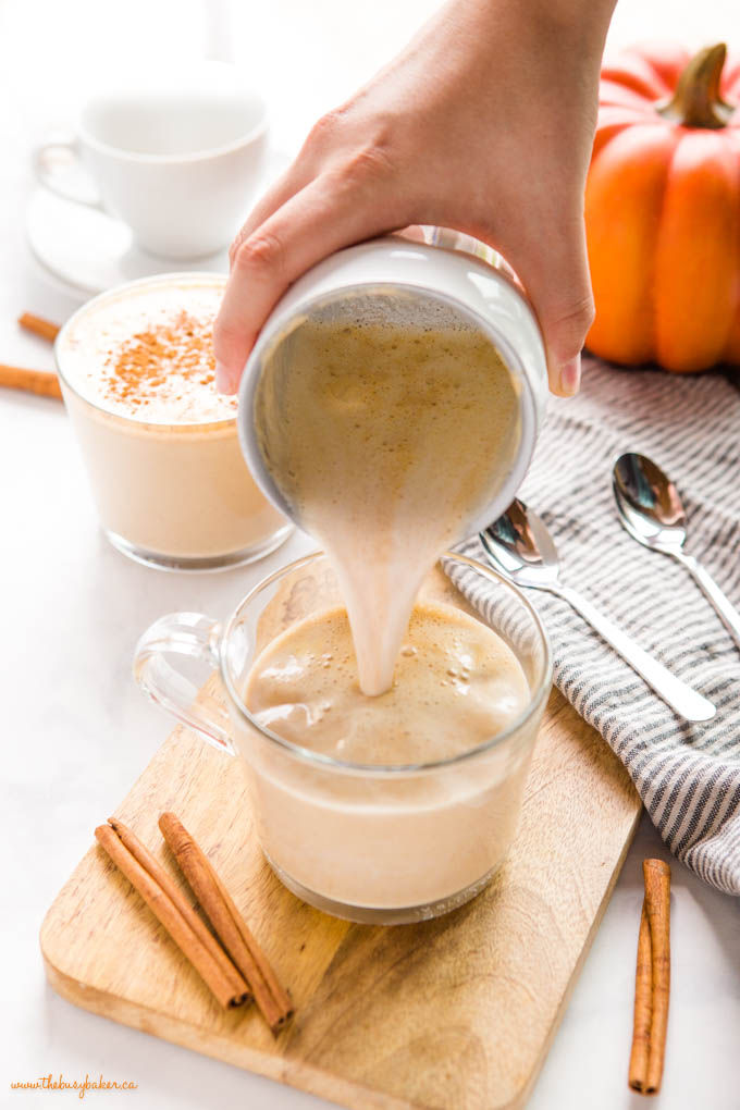 hand pouring foamed pumpkin spice milk into glass mug