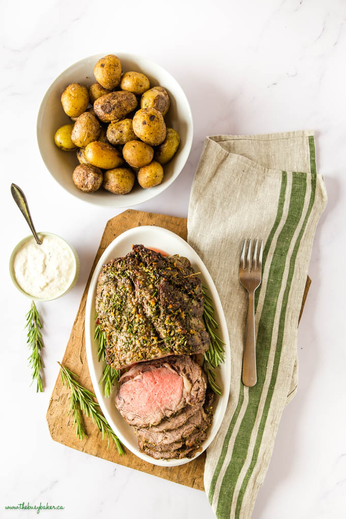 overhead image: prime rib on white platter with roast potatoes and horseradish sauce